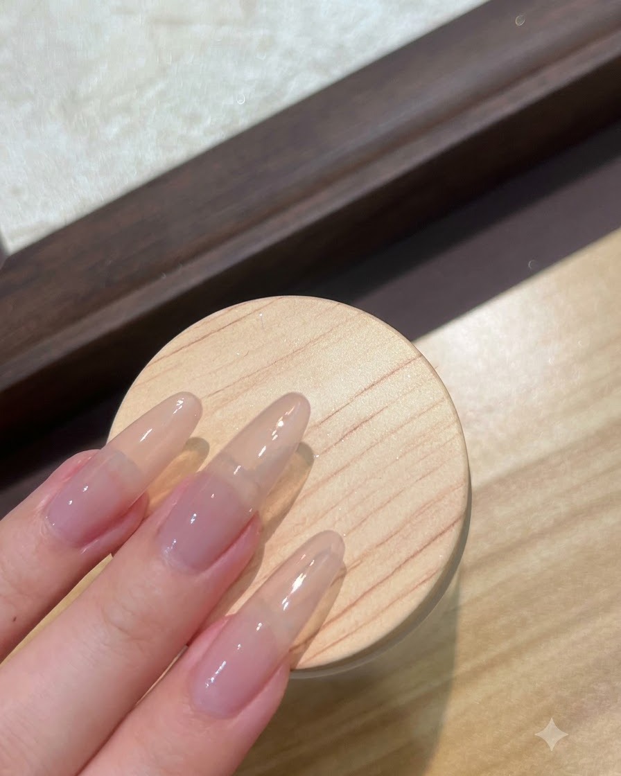 A close-up view of long nude extension nails being prepped with a clear base gel layer.