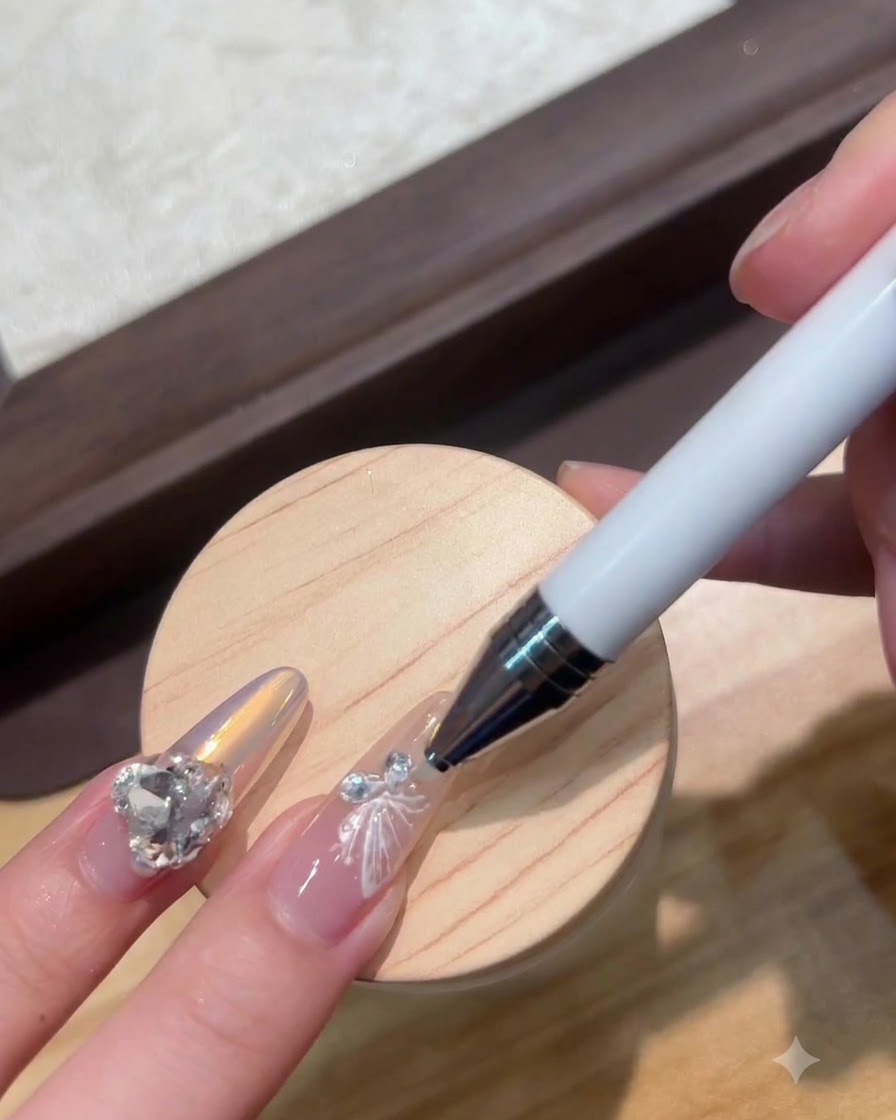 A dotting pen placing a tiny crystal next to a white butterfly nail charm.