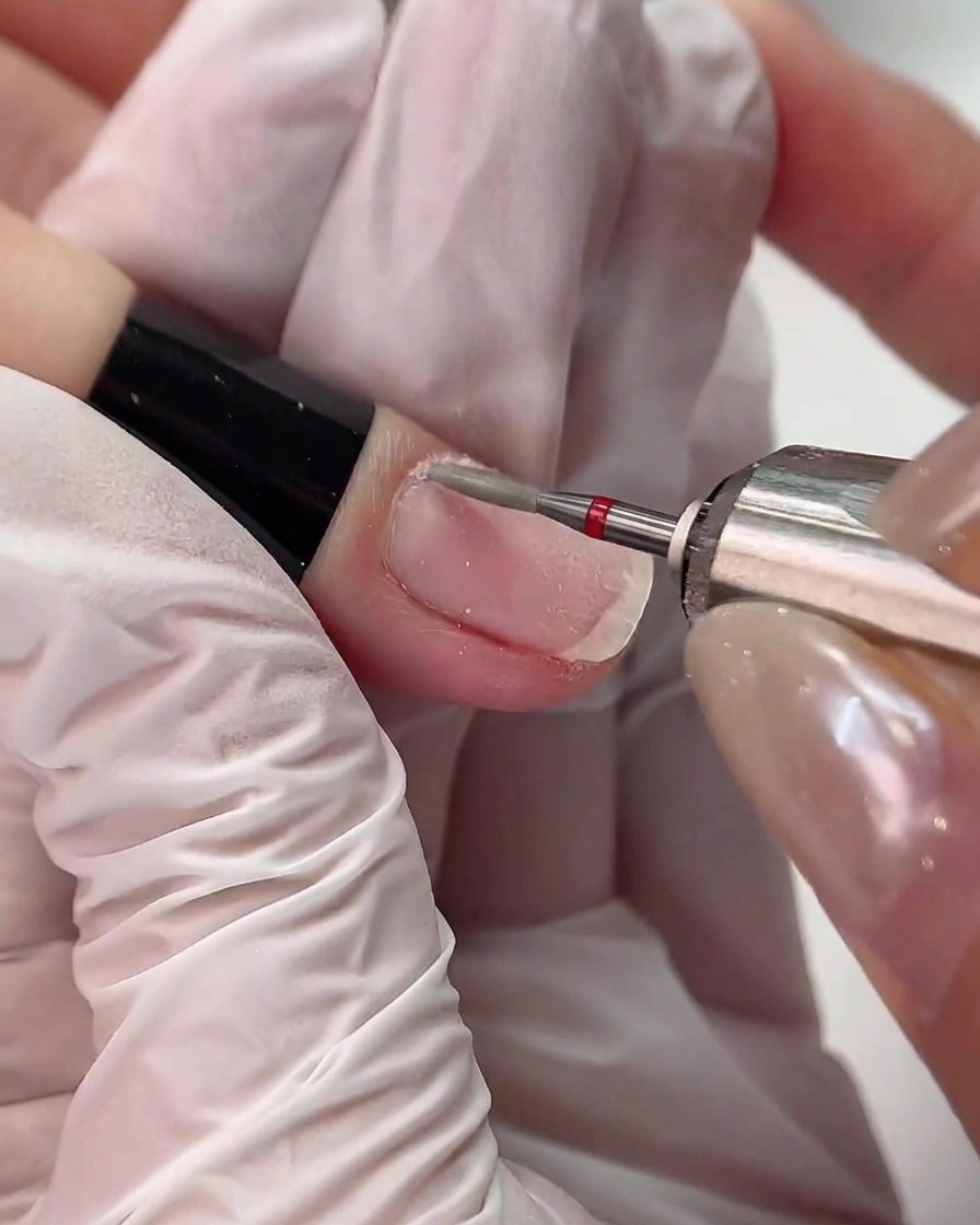 An e-file with a red-banded diamond drill bit working carefully along the cuticle line of a finger.