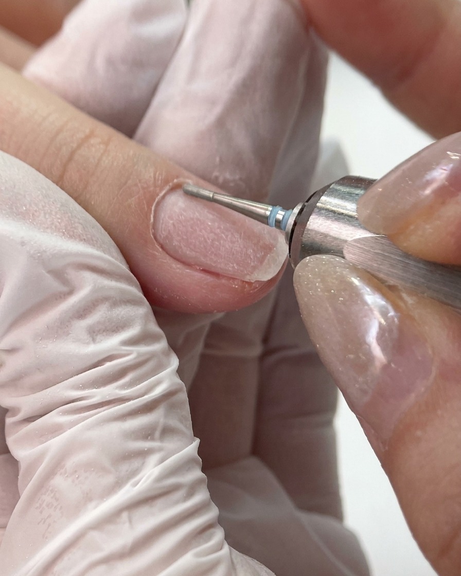 A small fine-grit e-file bit cleaning and smoothing the lateral fold and cuticle area of a nail.