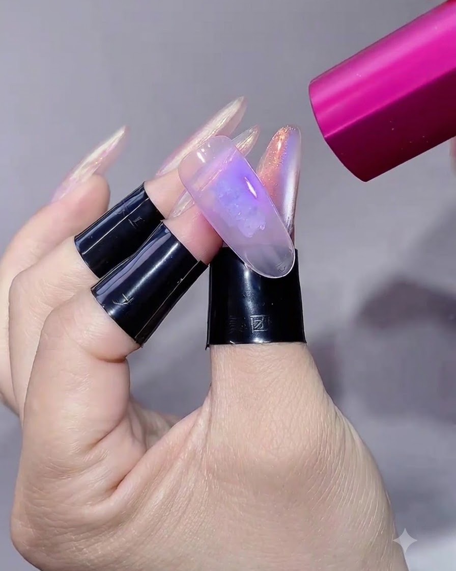 A pink handheld UV/LED lamp shining light onto a manicured nail extension.
