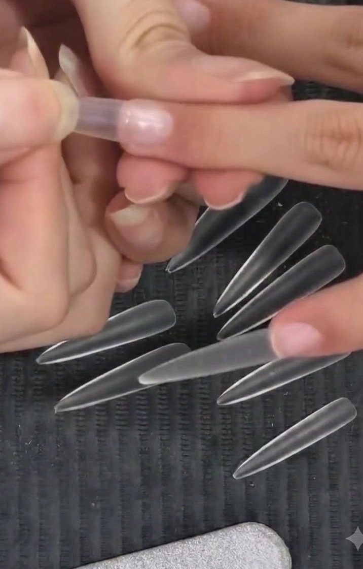 A technician pressing a clear almond nail tip onto a natural finger using a high-position placement technique.