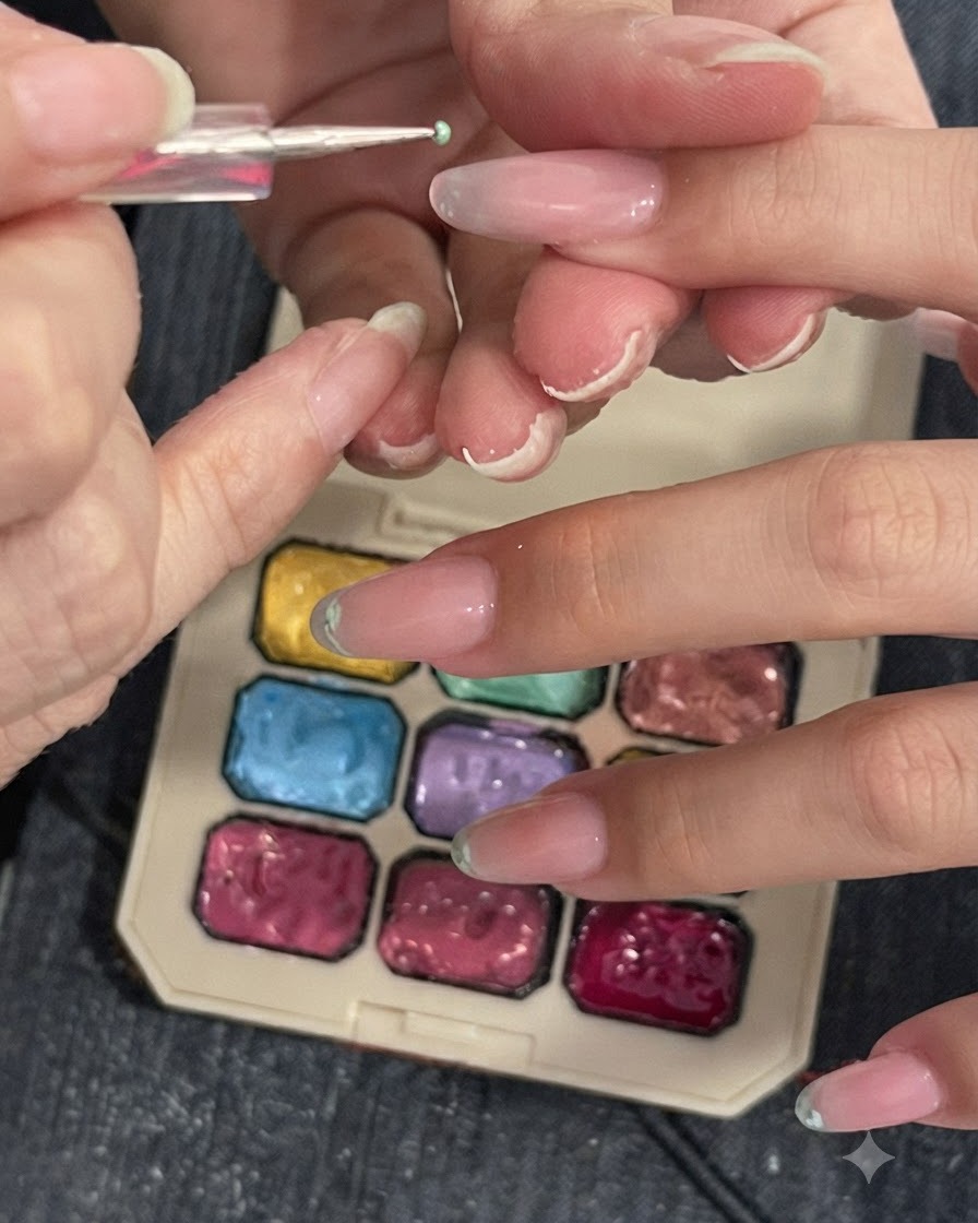 A detail tool or sponge dabbing light green pigment onto a nail tip next to a color palette.