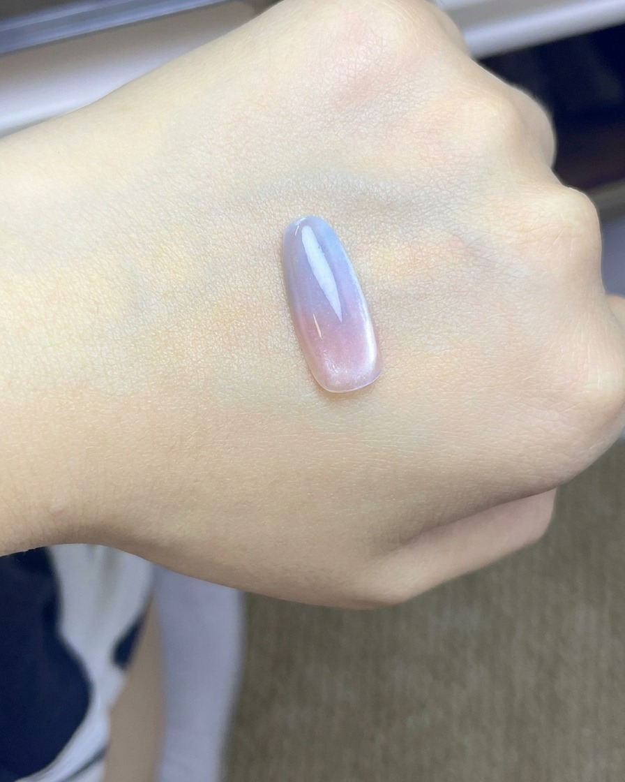 A nail tip with a pink blush gradient curing under a UV/LED lamp.