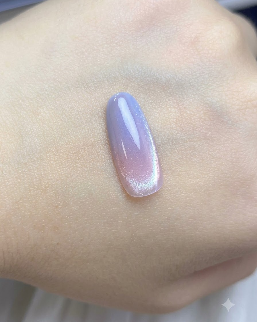 A brush applying a coat of sheer nude cat-eye polish over the gradient nail tip.