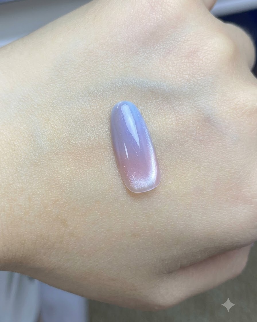 A brush applying a final glossy top coat over the completed pink and blue cat-eye nail design.