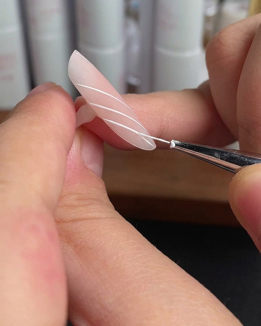 A ring finger nail with white parallel lines curing under a lamp light.