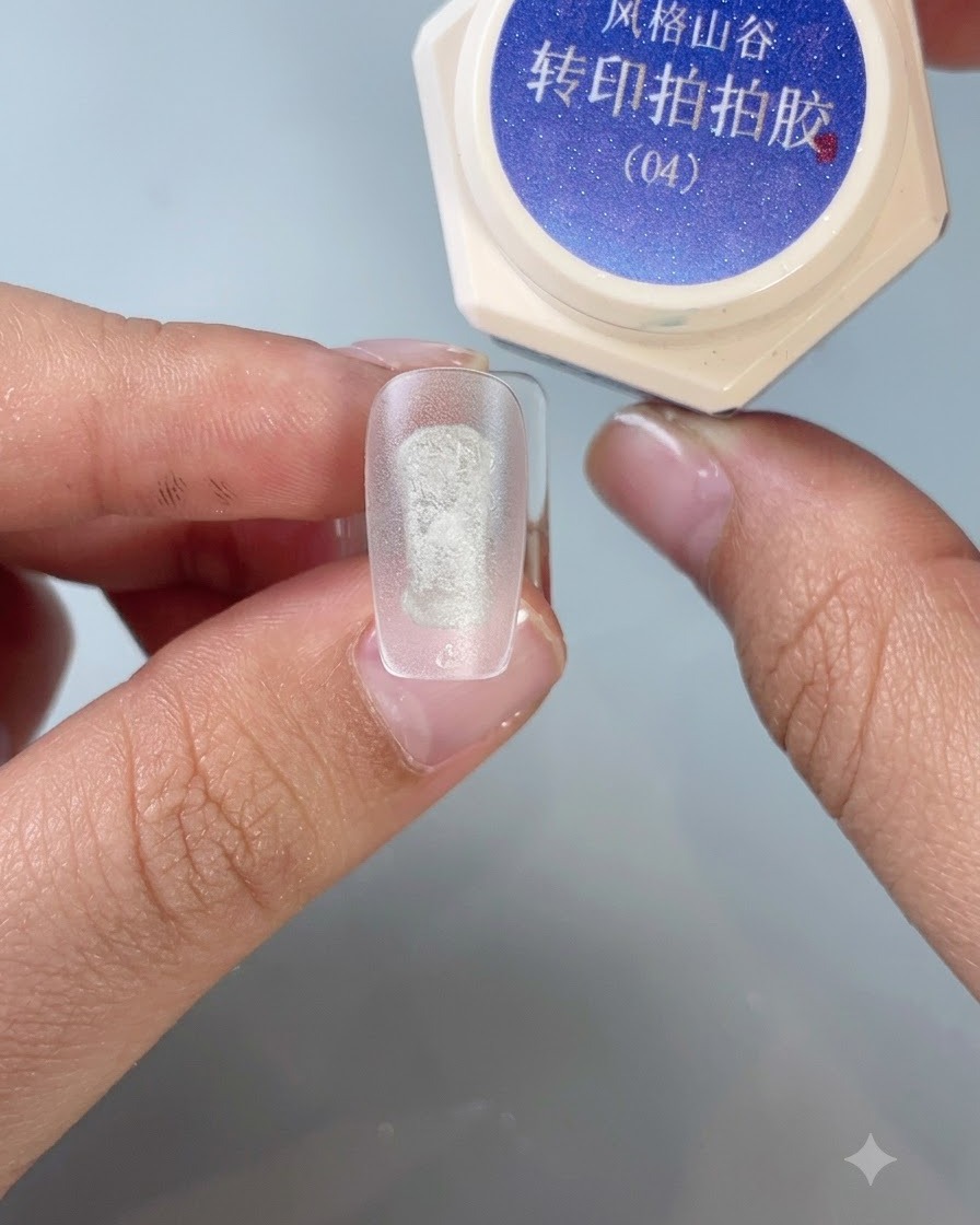 A brush applying transfer stamping gel No. 4 onto the center of a frosted practice nail tip.