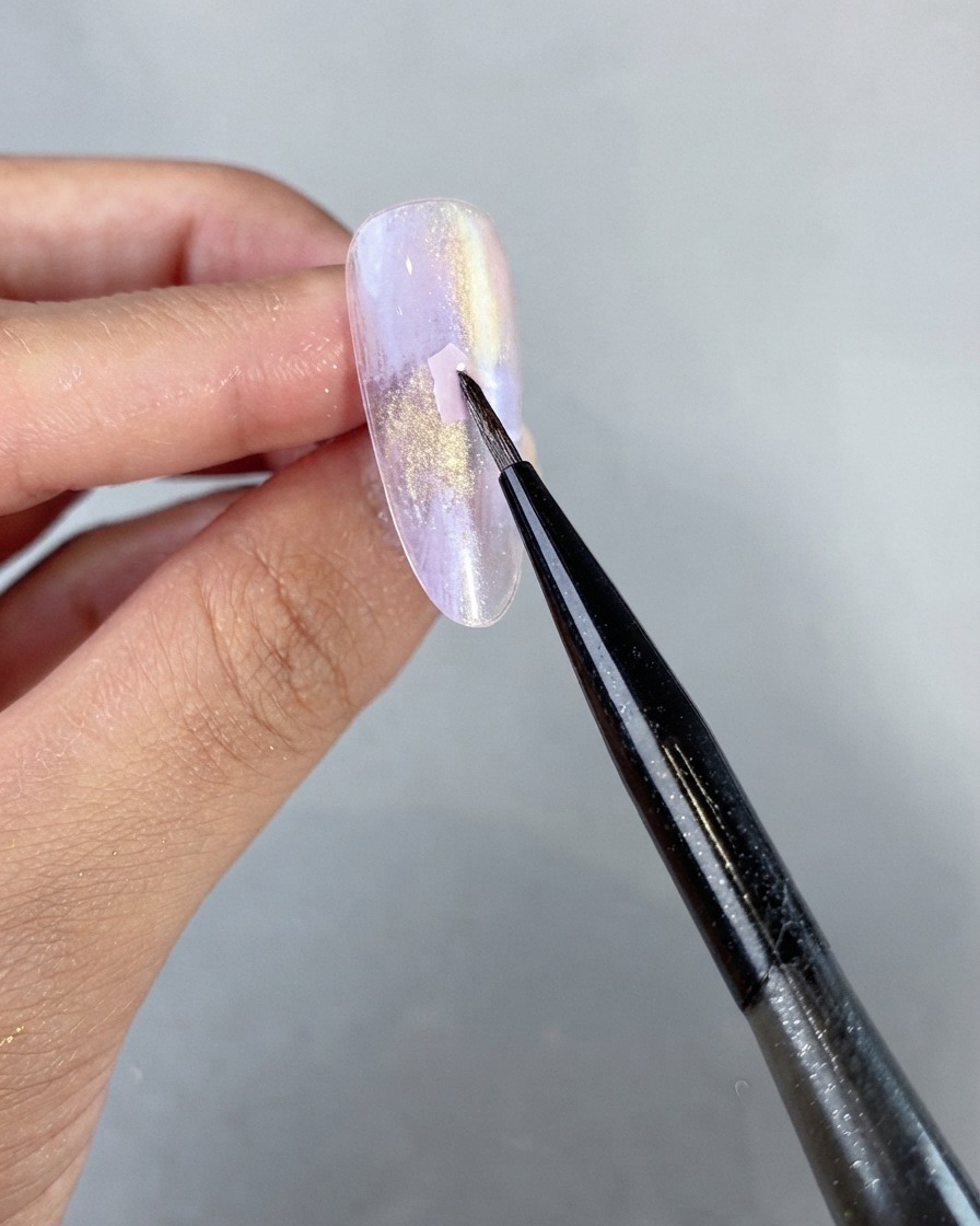 A fine art liner brush delicately placing a pink shell piece onto an uncured purple pearlescent gel nail surface.