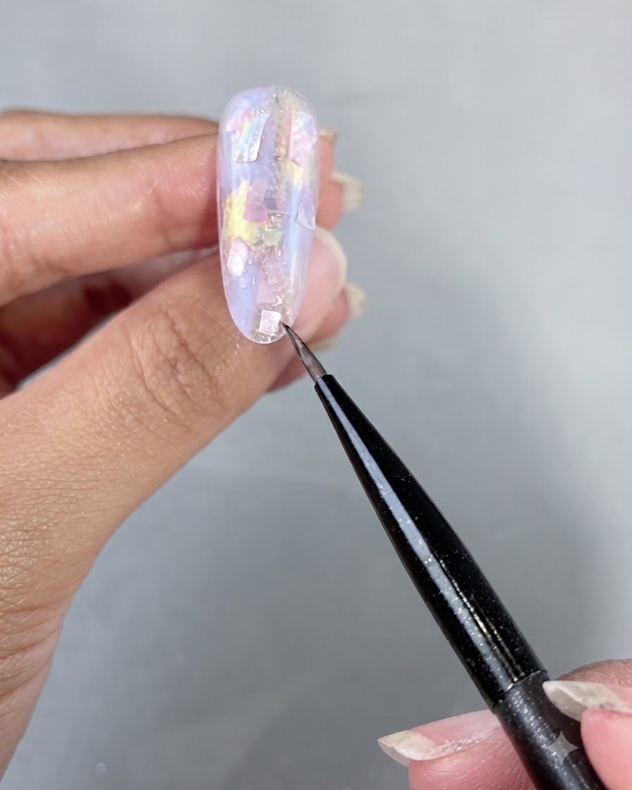 A hand placed under a UV LED nail lamp curing the applied shell pieces and builder gel.