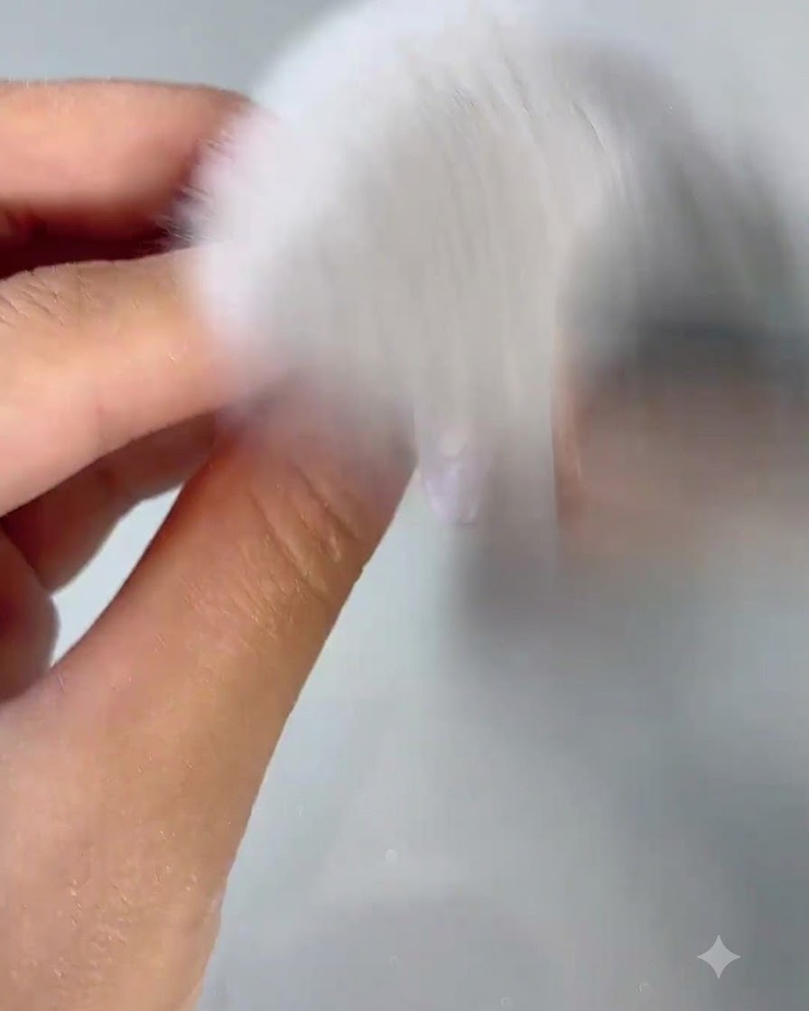 A fluffy white dusting brush sweeping away nail dust from a freshly buffed nail.