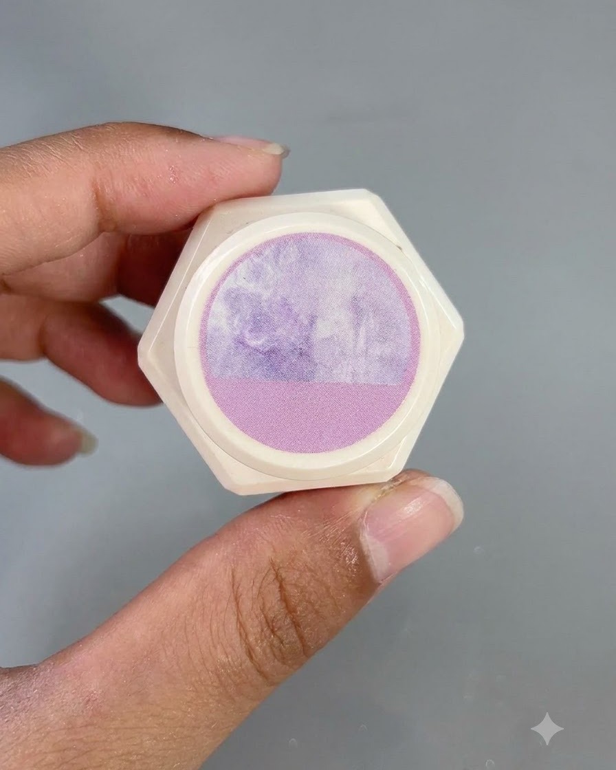 A hexagonal white container with a purple watercolor pattern sticker on the lid, held up by fingers.