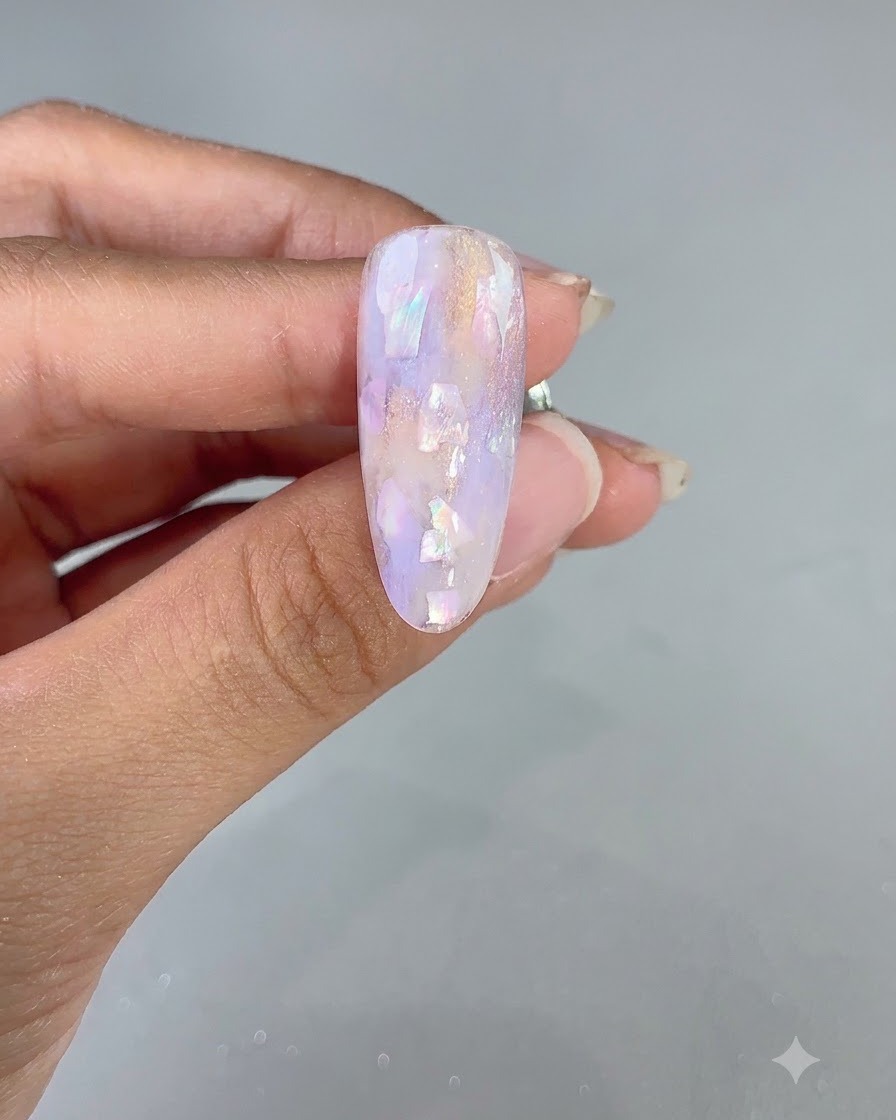A close-up of a decorated purple and shell-encrusted nail after flash curing.