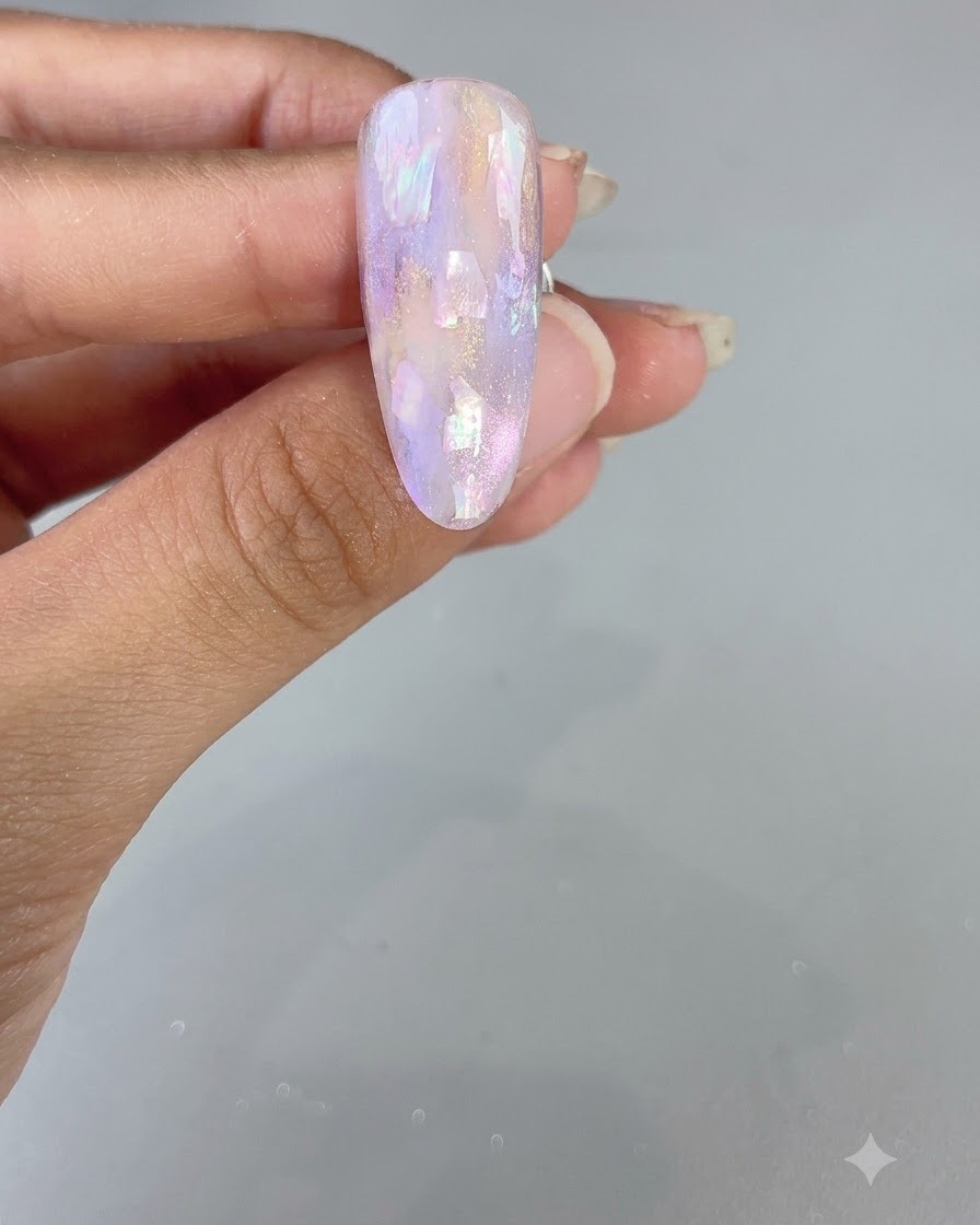 A finished almond-shaped nail featuring a glossy purple watercolor and shell design.