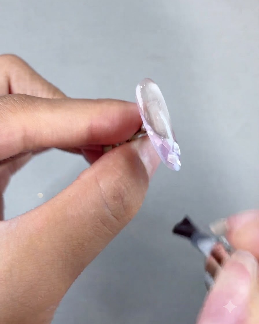 A brush applying soft builder gel over a decorated nail extension before curing.