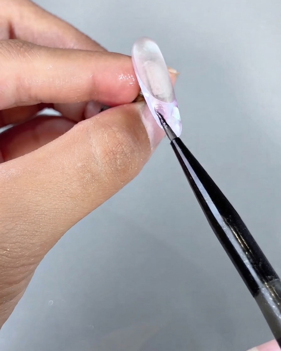 A fine brush applying magical sea cat eye gel onto a specific section of a textured nail design.