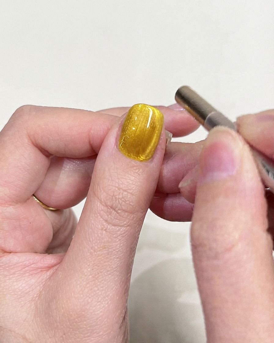 A detailed inspection shot of a yellow cat-eye gel nail focusing on the magnetic light reflection.