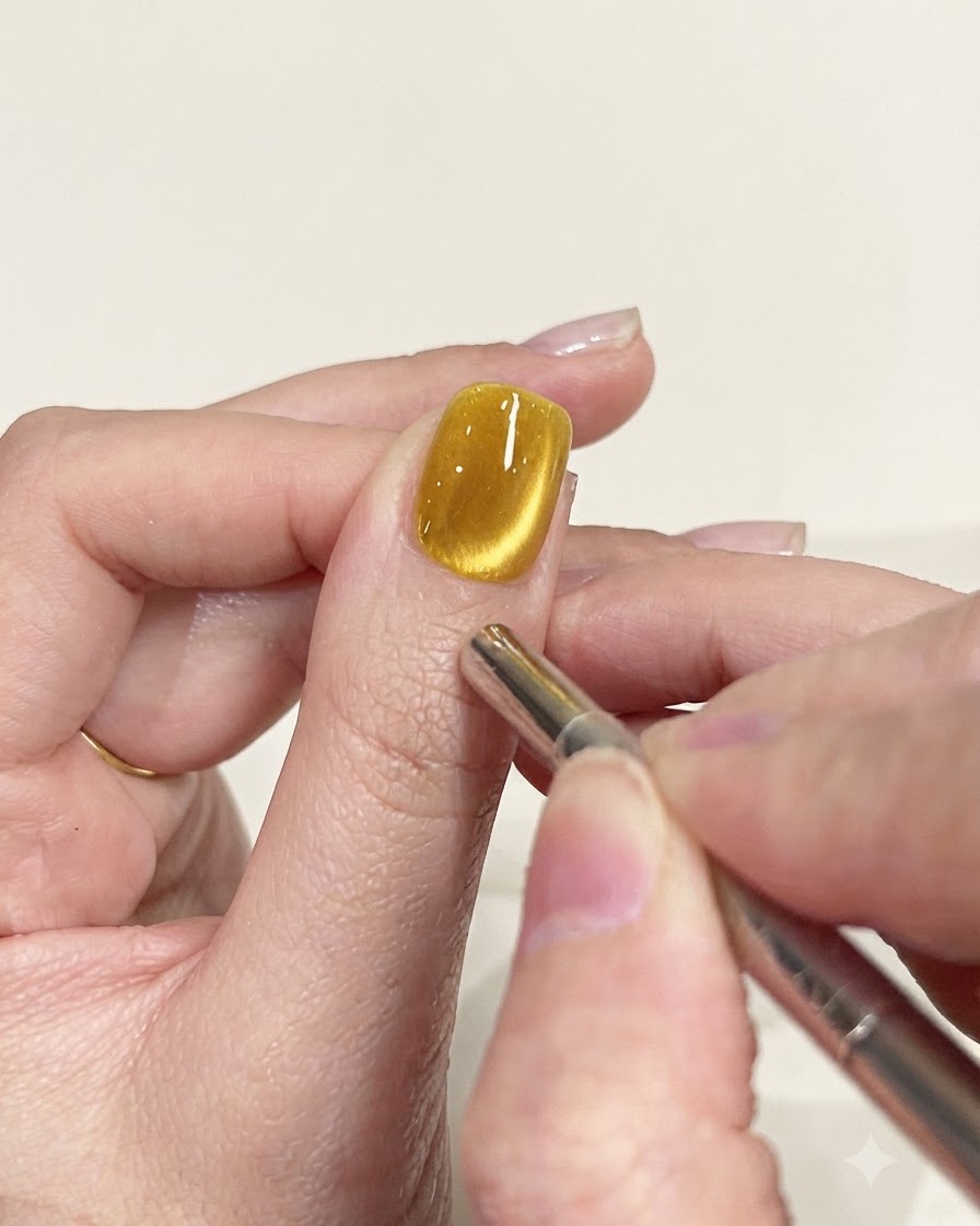 A precision magnet pen tool being used to refine the shimmer path on a yellow cat-eye nail.