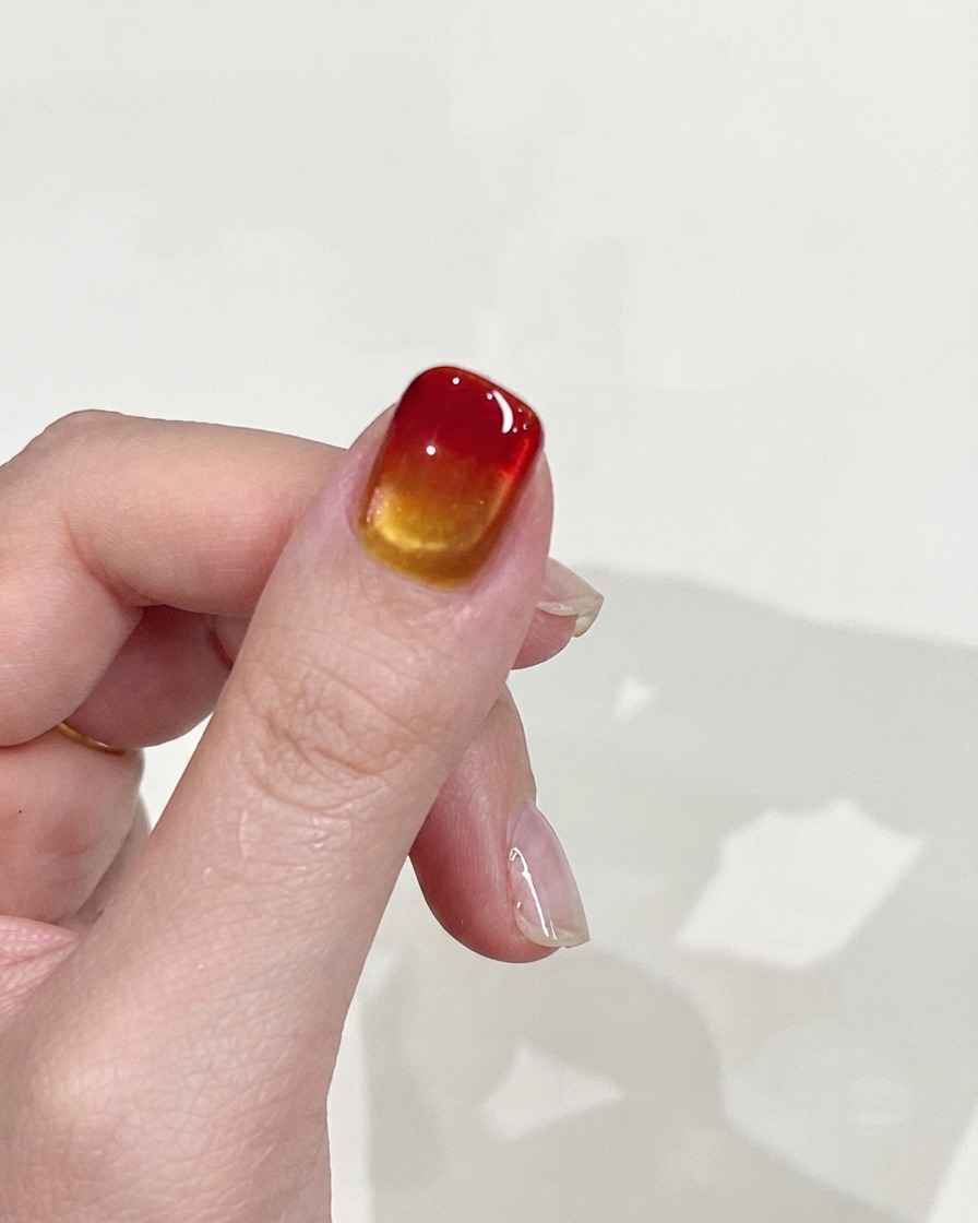 A hand held up against a plain background, displaying the smooth gradient texture and glossy finish of the nail.