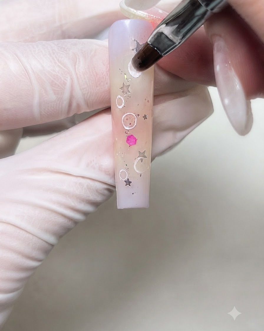 A nail art brush softly blending the inner borders of white cream circles on a gradient nail.