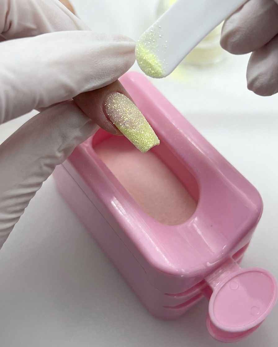 A small dust brush sweeping excess glitter powder off a finished glitter nail surface.