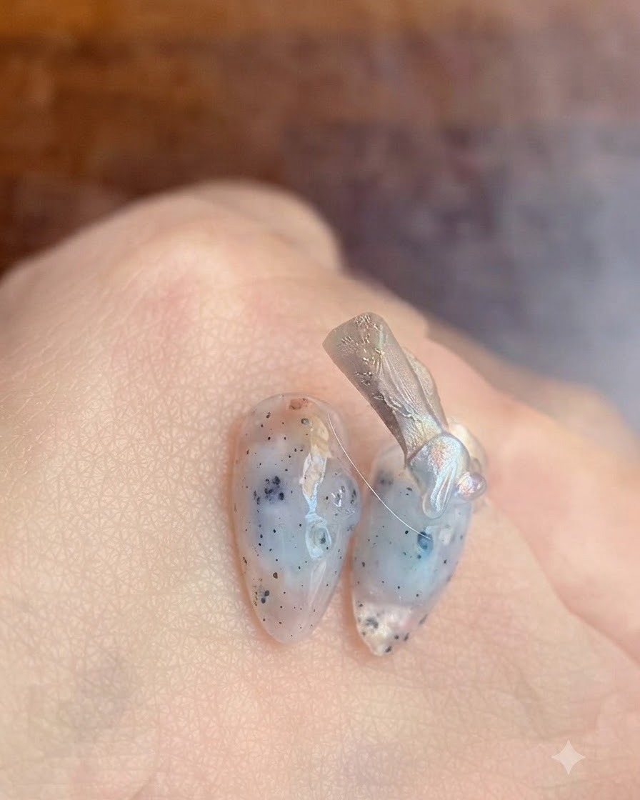A close-up of a nail brush applying a clear base coat gel onto a natural fingernail.