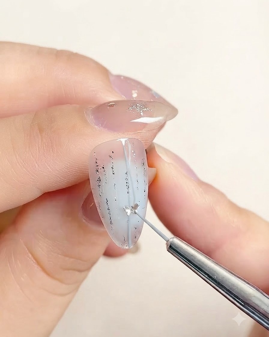A precision tool placing a small star-shaped sticker along the center line of a decorated fingernail.