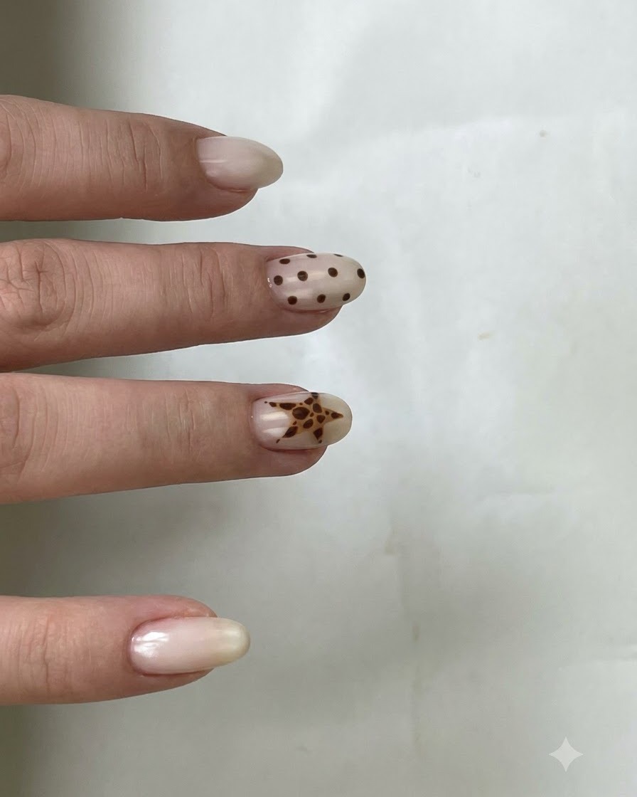 A brush applying clear top coat over a nail featuring brown polka dots and a star design.
