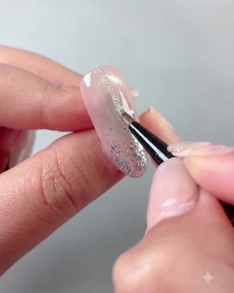 A fine liner brush drawing thin silver glitter lines on a cured nail surface.
