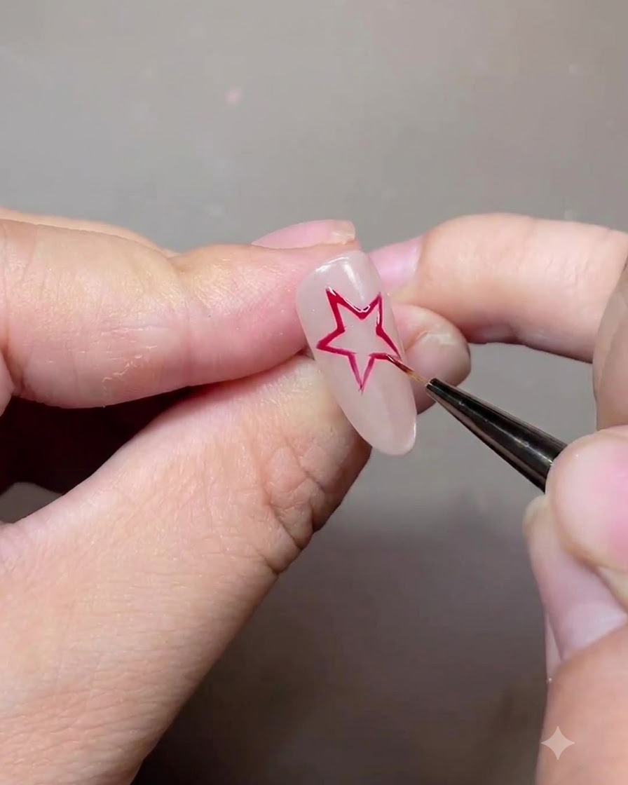 A fine liner brush drawing a red five-pointed star outline on a nude gel nail.