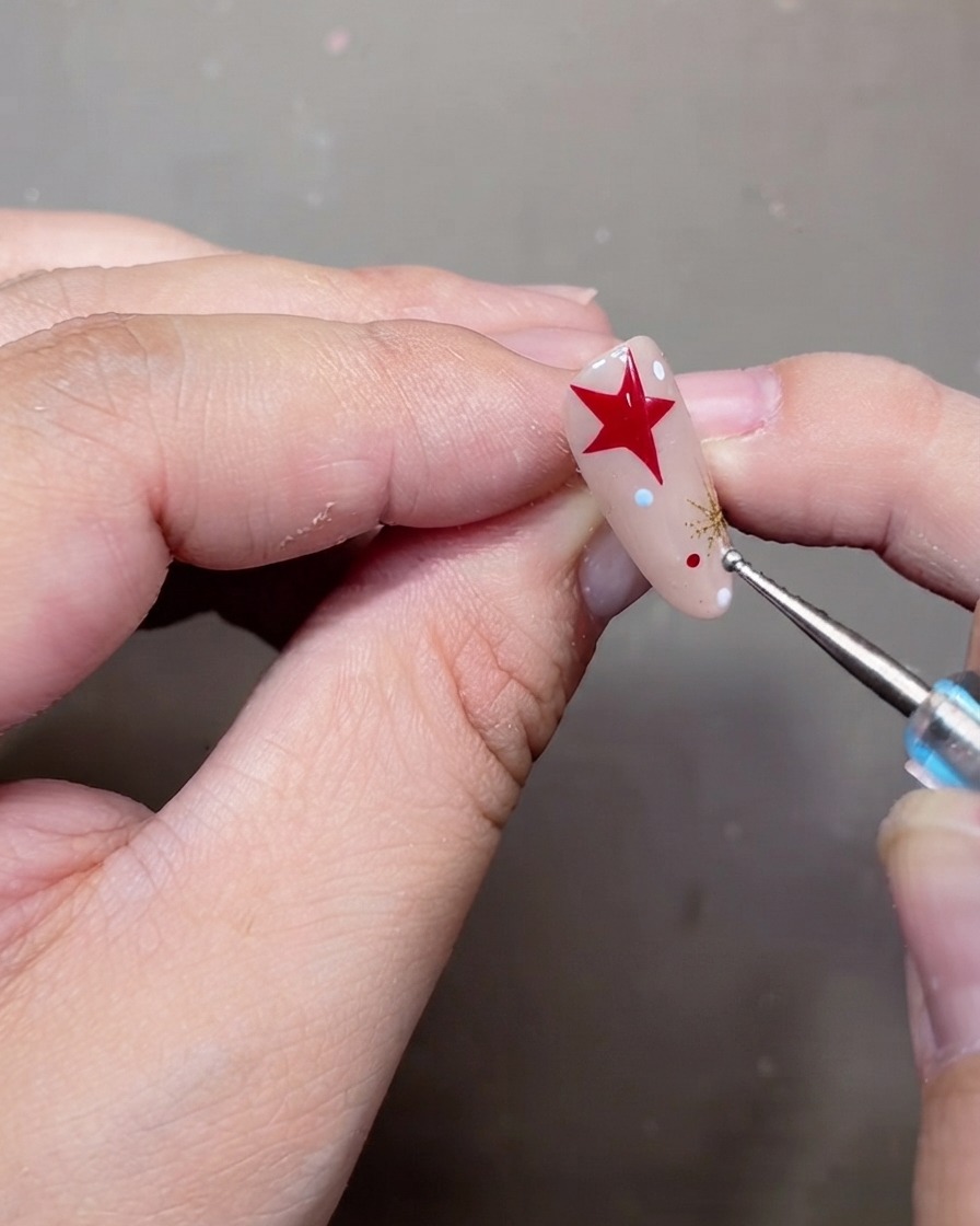 A dotting tool placing tiny white and red polka dots onto a decorated nude gel nail.