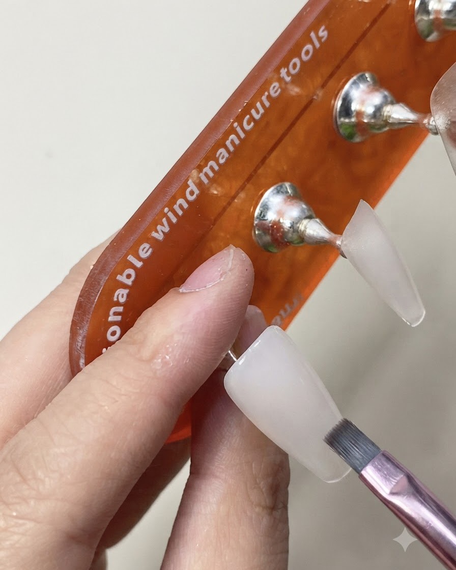 A brush applying a glossy top coat layer onto the cured milky white nail extension.