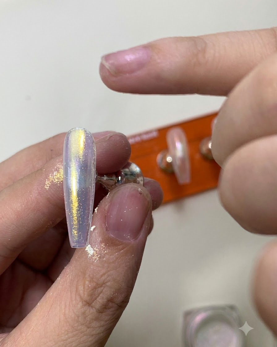 A silicone applicator tool rubbing shimmering aurora chrome powder onto a glossy nail surface.