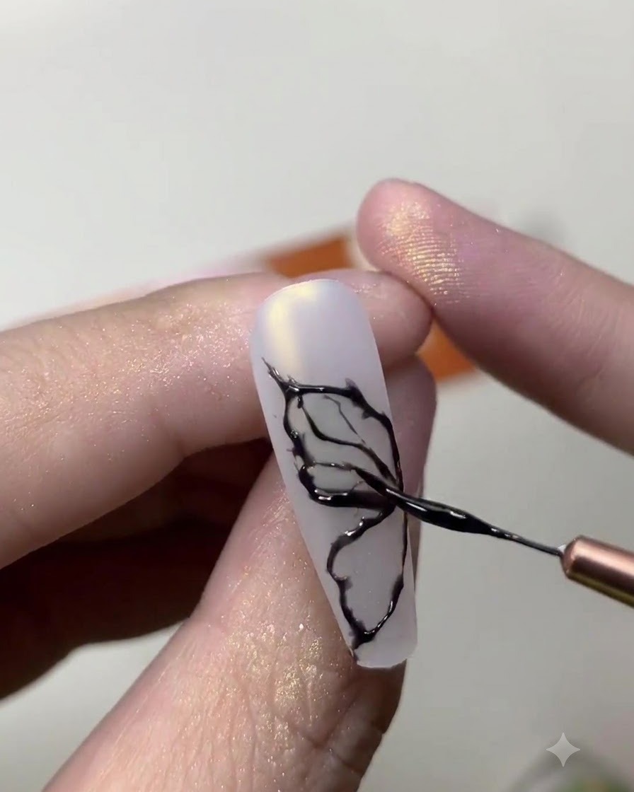 A close-up of a nail artist using a fine brush to draw delicate black butterfly wing lines on a milky white nail.