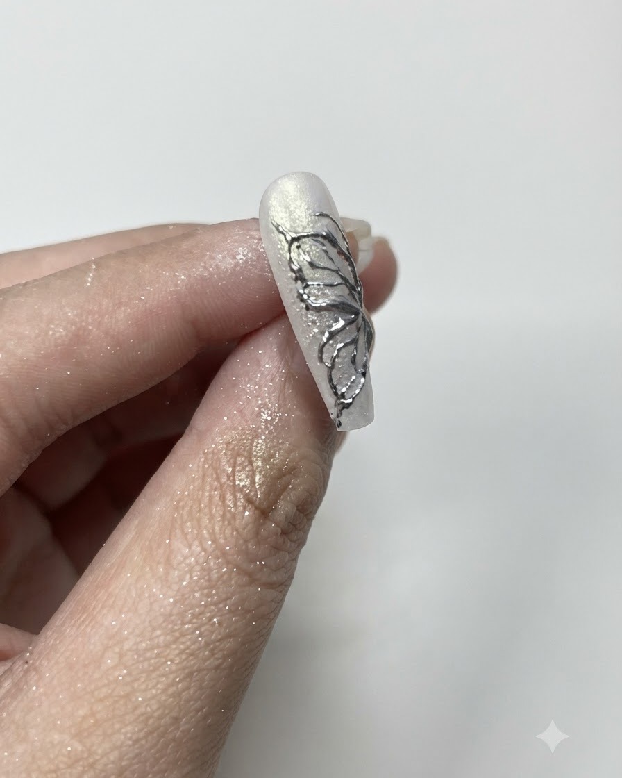 A fluffy brush cleaning away excess silver chrome powder from the edges of a manicured nail.