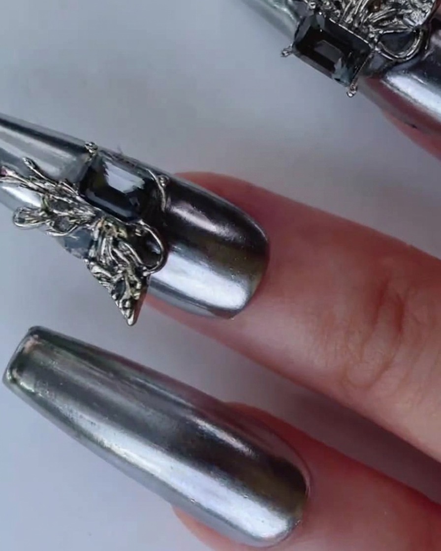 A hand tilting a silver chrome nail under bright lighting to highlight its dynamic reflective mirror finish.