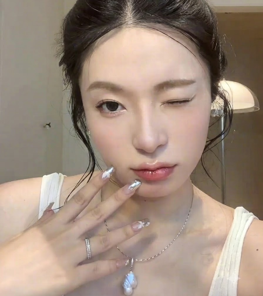 Close-up of a hand with silver chrome nail art held near the face with a winking expression.