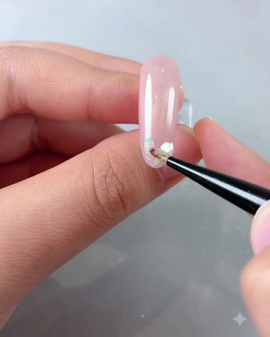 A fine brush placing iridescent cloud powder flakes onto the front edge of a glossy pink nail.