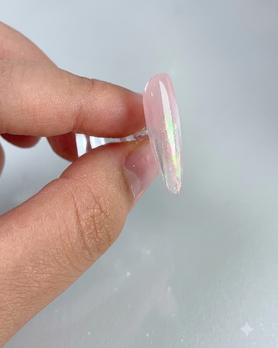 A close-up of a glossy pink nail showing a shimmering aurora effect after brushing away excess powder.