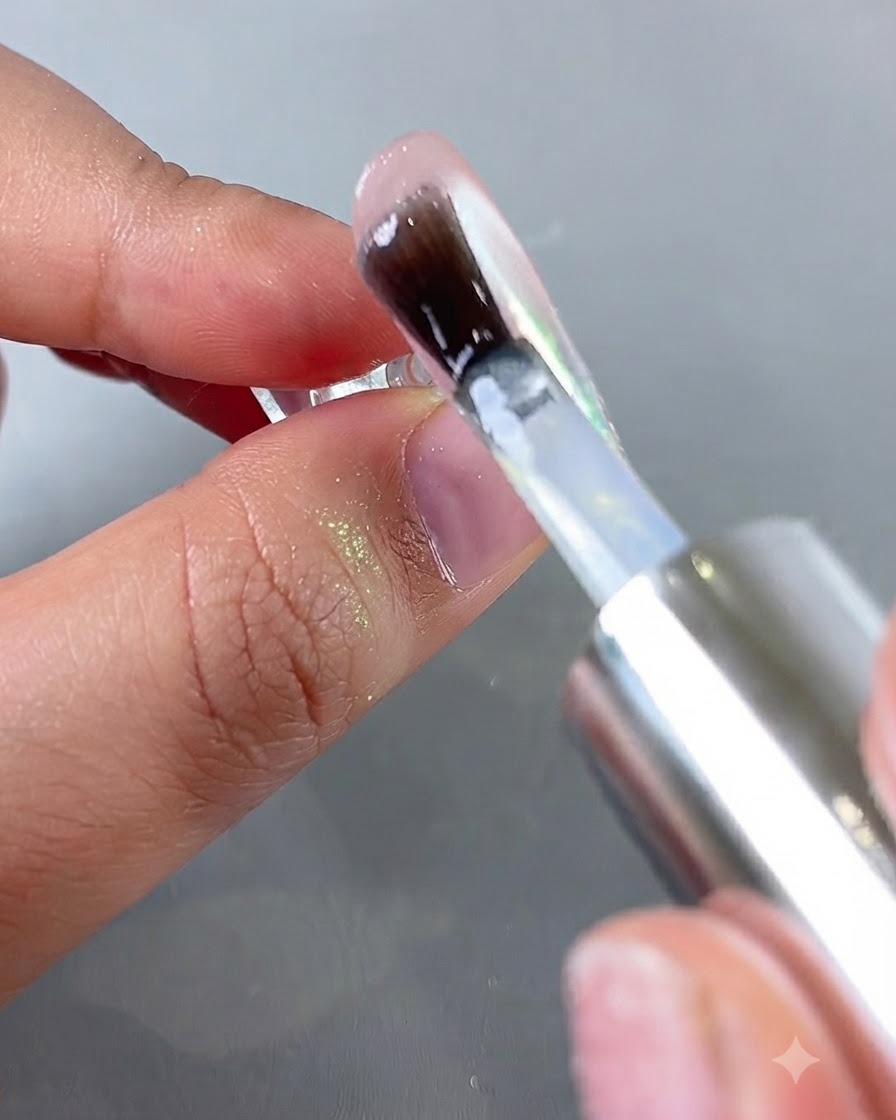 A brush applying a clear top coat over a shimmering aurora chrome nail surface.