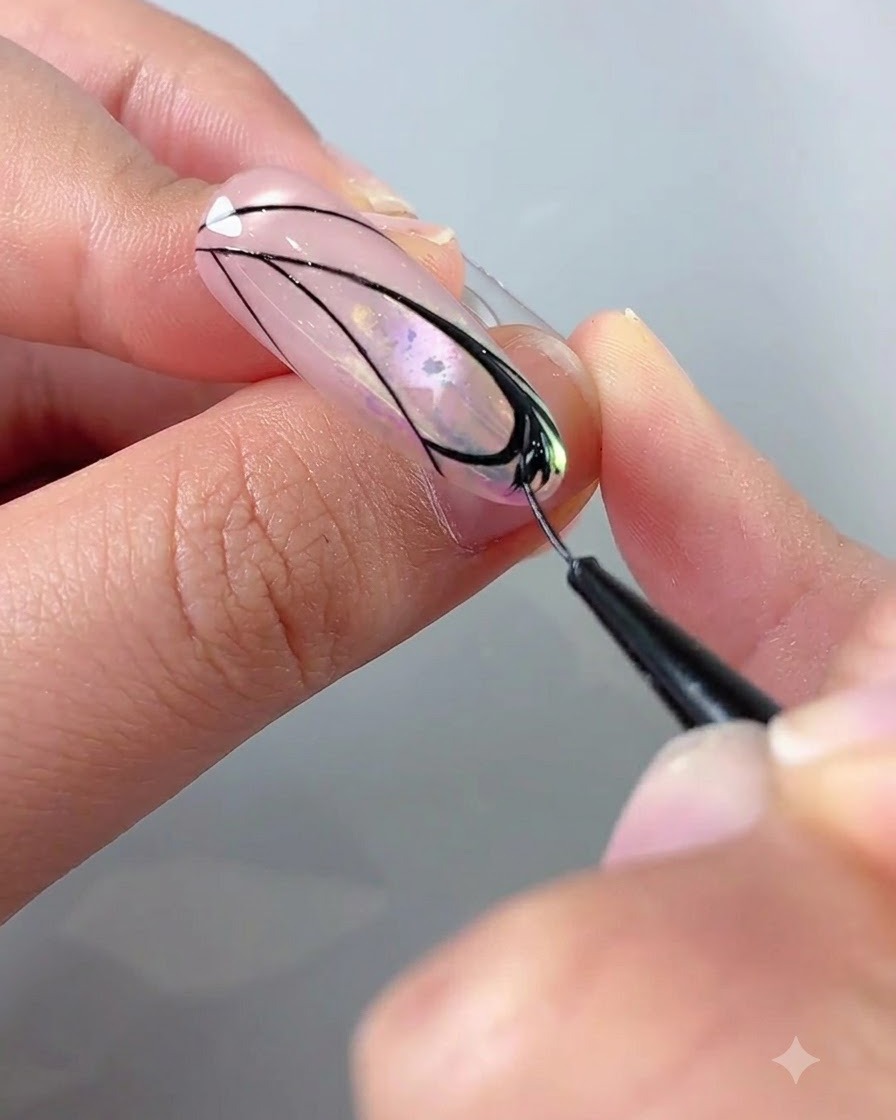 A close-up of a hand using a liner brush with black gel to fill in details inside a butterfly wing design on a nail.