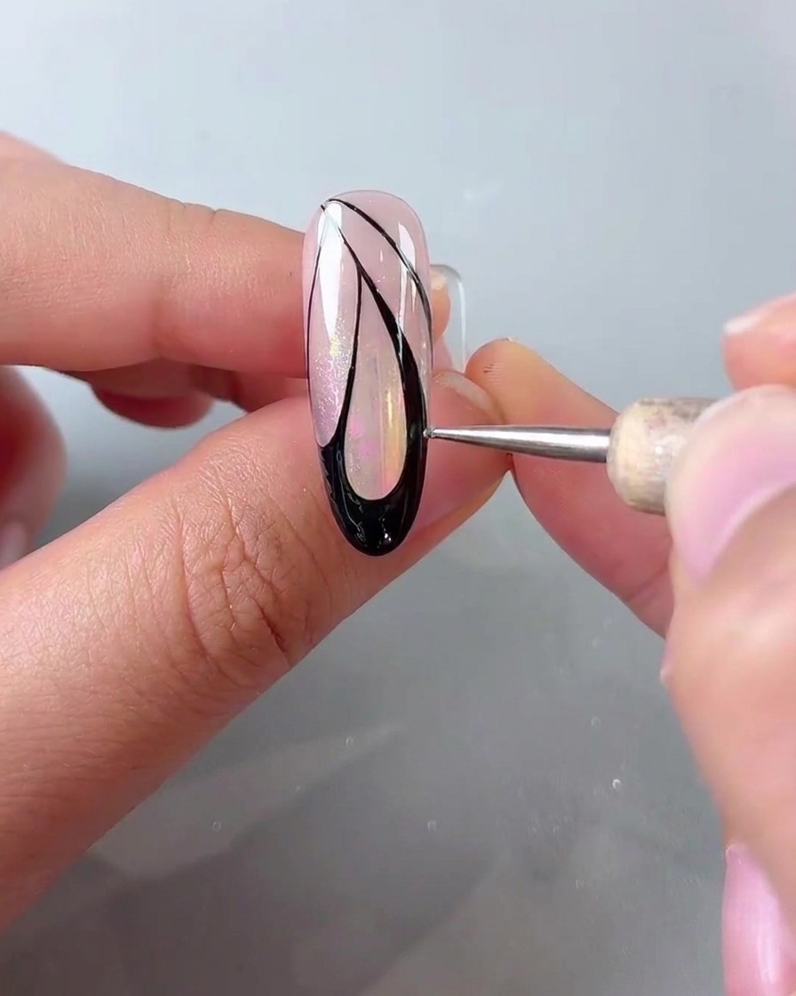 A dotting pen placing small white dots along the outer edge of black butterfly wing nail art.