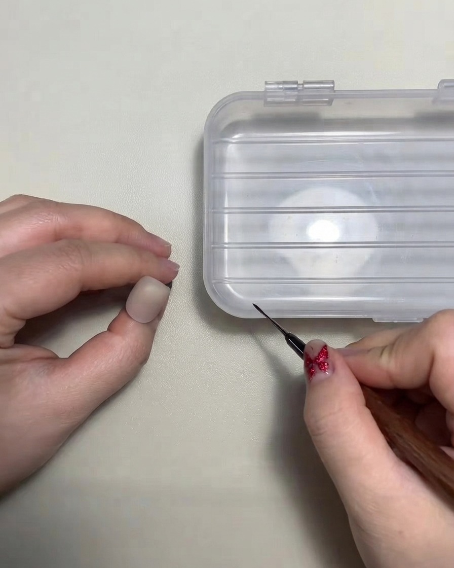 A nail artist holding a fine liner brush near a practice nail tip.