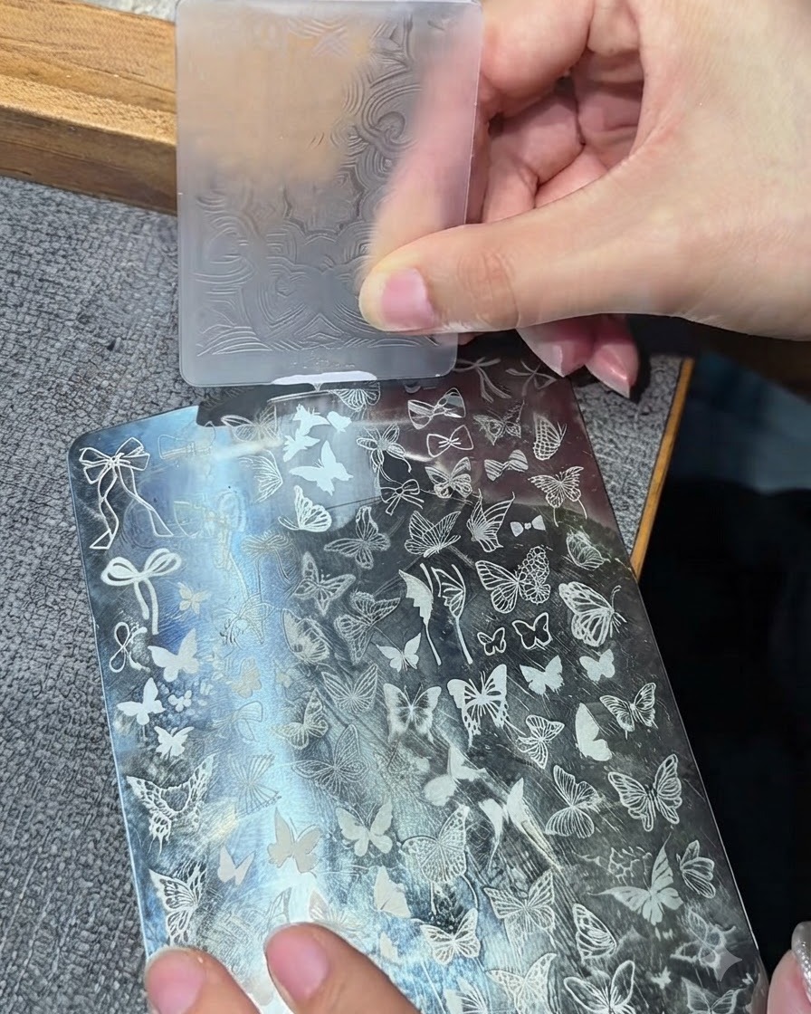 A clear silicone stamper head pressing onto a metal stamping plate to pick up a white design.