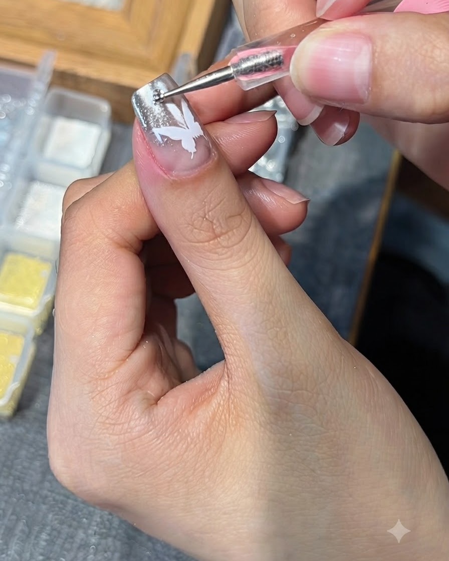A dotting tool placing a small rhinestone onto a nail featuring a white butterfly design.