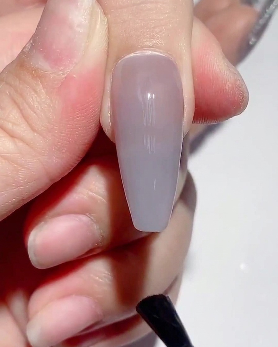 A brush applying matte top coat onto the surface of a painted nail.