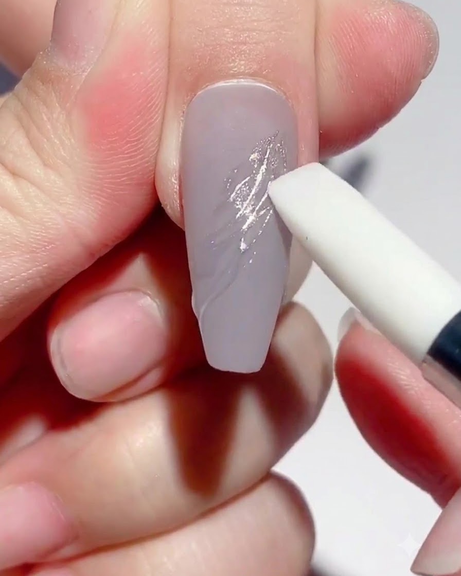 A silicone pen tool rubbing silver mirror powder onto cured gel line art on a taupe-colored nail.