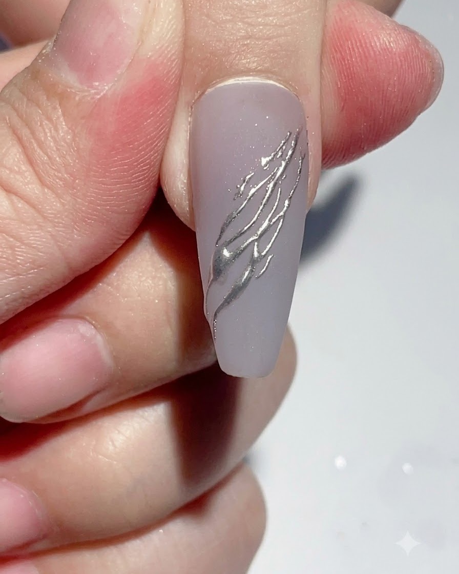 A liner brush applying a small dot of clear rhinestone glue onto a decorated nail.
