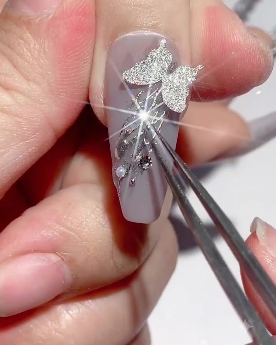 A pair of tweezers holding a charm while rhinestone glue is applied around nail decorations.