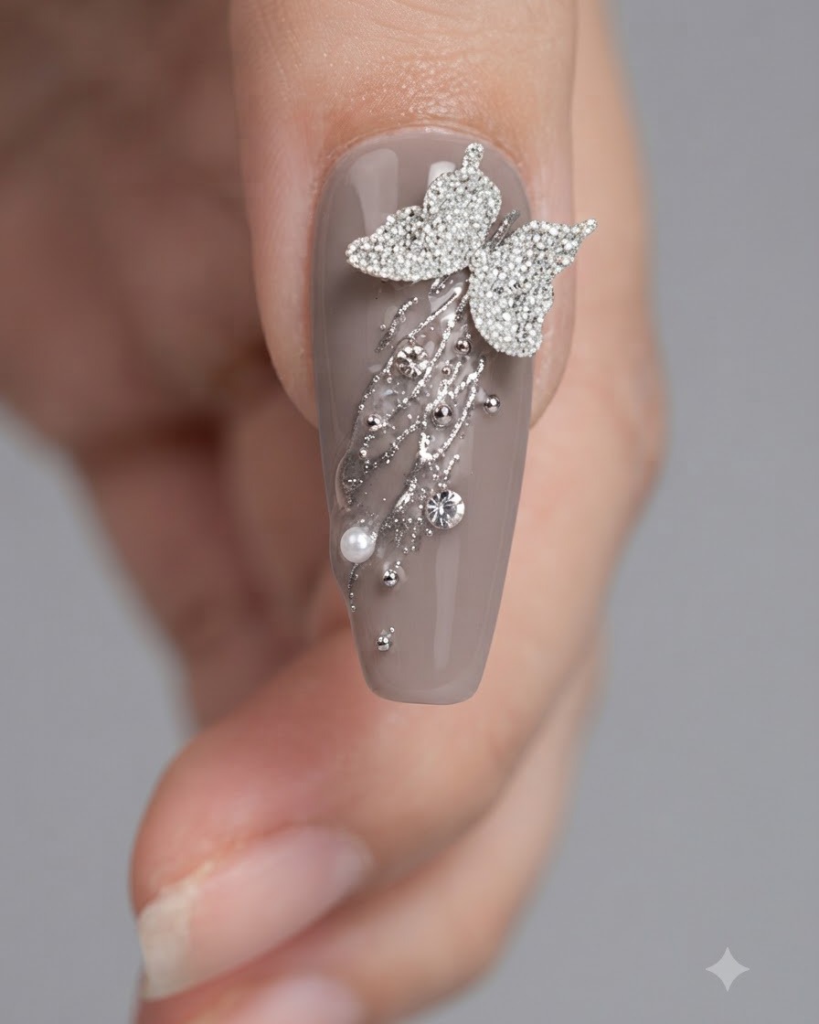 A close-up of a nail brush applying top coat around butterfly and rhinestone decorations on a grey nail.